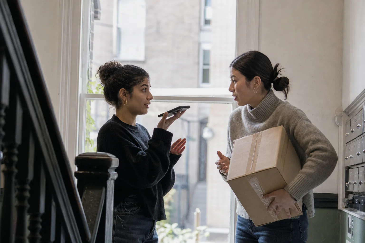 Two people having a face-to-face conversation in a home setting, one holding tools, while a phone sits nearby translating their discussion